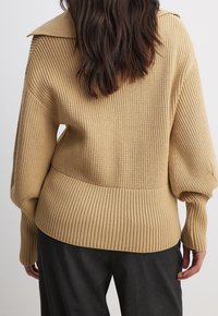 Maglione a coste beige con colletto a risvolto, maniche a palloncino e vita aderente, che presenta un motivo testurizzato in tutto il capo.