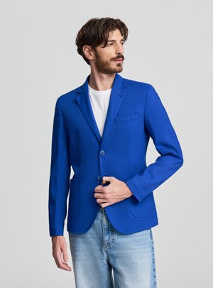 Blazer blu, design monopetto, due tasche frontali e rever. Realizzato in tessuto strutturato, abbinato a una t-shirt bianca e jeans.