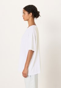 Maglietta bianca oversize con maniche corte, realizzata in tessuto leggero. L'orlo è dritto, con una vestibilità rilassata e un design semplice.