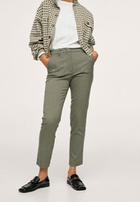 Veste à carreaux verts et blancs portée sur un haut blanc, associée à un pantalon vert à carreaux et coupe slim, avec des mocassins noirs.