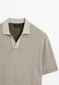 Polo maglietta lavorata a maglia in cotone color taupe chiaro. Presenta un collo a V e maniche corte con polsini a costine. Tessuto morbido e traspirante.