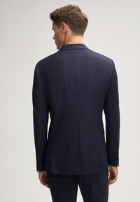 Marineblaues Sakko mit Reverskragen, einzelnen Rückenbelüftung und strukturierter Schultergestaltung. Glattes Gewebe mit subtiler Textur.