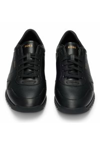 Czarne skórzane trampki z teksturowanymi i gładkimi panelami, sznurowanym przodem, gumową podeszwą oraz złotym napisem "BOSS" na języku.