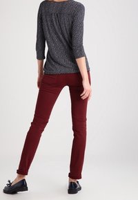 Námořnický top s bílým puntíkovým vzorem a tříčtvrtečními rukávy. Bordó slim-fit kalhoty s ohrnutými manžetami. Černé ploché boty s detailem mašle.