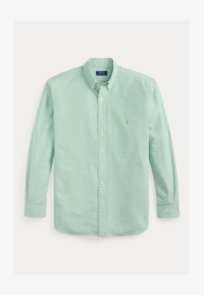 Gai zaļš kokvilnas krekls ar pogām, garām piedurknēm, apkakles izgriezumu un mazu izšūtu logo kreisajā krūtīs.