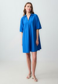 Abito blu a maniche corte con colletto, caratterizzato da una vestibilità ampia e un orlo fino al ginocchio. Tessuto liscio con un colore uniforme e un design sottile.