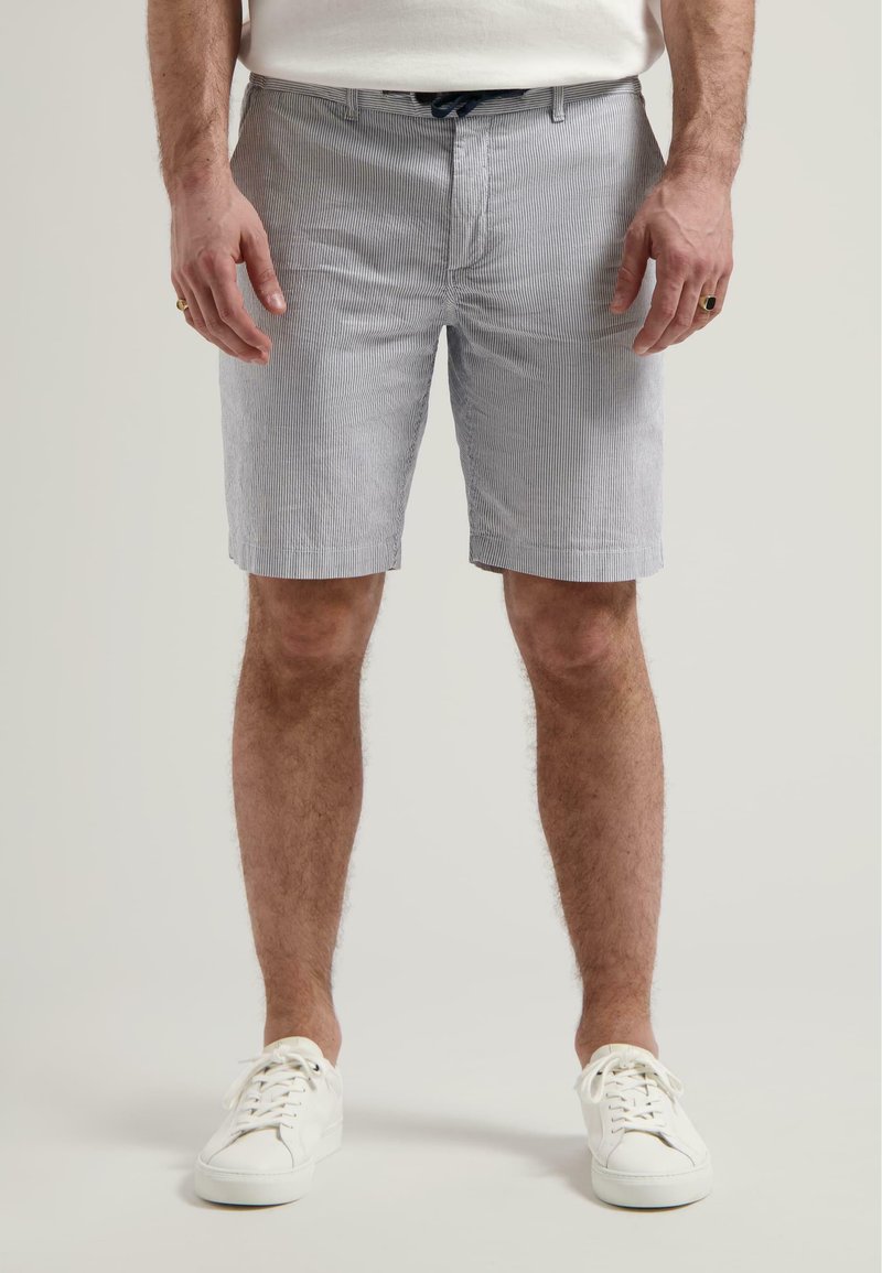 Shorts pour hommes en bleu clair avec des rayures verticales blanches, fabriqués en tissu texturé. Présentent un fermoir à l'avant et des passants de ceinture, associés à des baskets blanches.