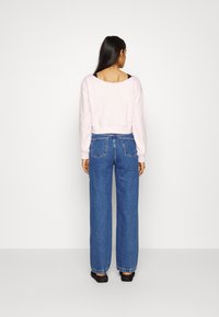 Sweatshirt rosa claro, cropped, com mangas longas, combinado com jeans de corte largo em denim azul, de cintura alta, com bolsos traseiros e pernas retas.