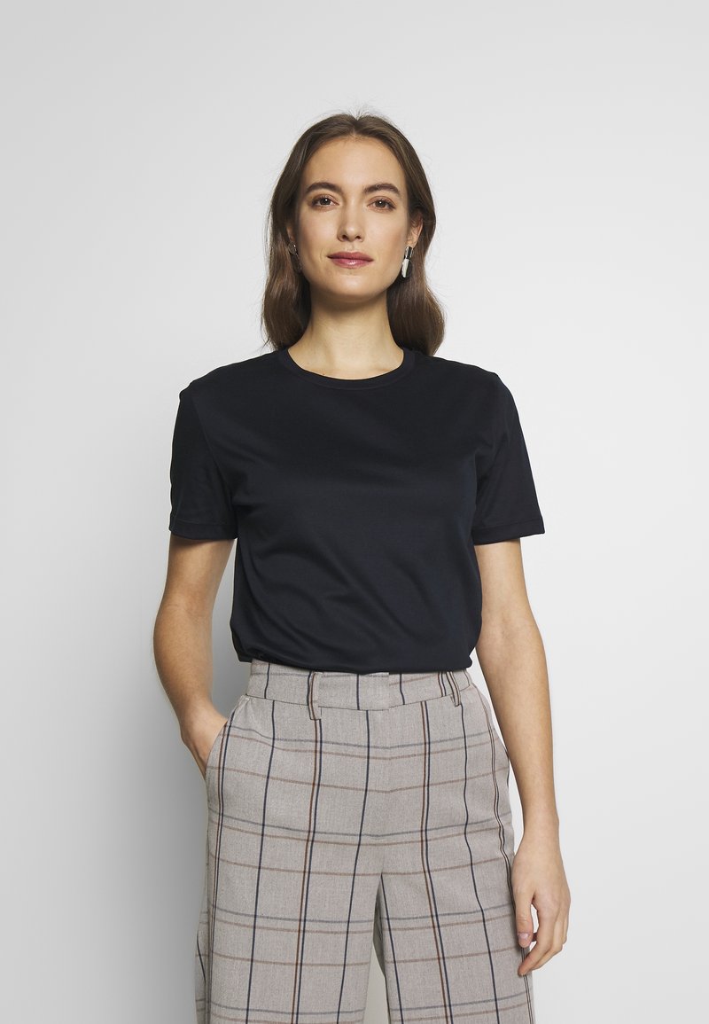 Schwarzes kurzes T-Shirt aus glattem Stoff, kombiniert mit grauen karierten Hosen mit braunen und marineblauen Linien, ausgestattet mit seitlichen Taschen.