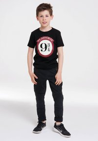 Black t-shirt with a round graphic featuring the text "PLATFORM 9¾" in red and white. Paired with black pants and black sneakers.