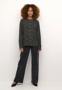 Chemise à manches longues imprimée noire et marine avec un col rond, associée à un pantalon large taille haute noir et des talons.