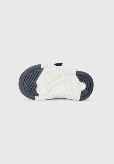Suela de zapatilla de goma en color navy con acentos blancos, que presenta patrones de tread texturizados y un diseño de talón redondeado. Logotipo visible cerca del talón.