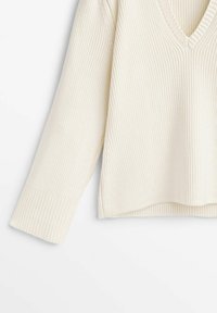 Pull en tricot de couleur crème avec un col en V, des manches longues, une texture côtelée et une coupe décontractée, présentant un ourlet légèrement cropped.