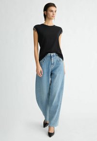 Top nero a maniche corte con vestibilità rilassata, abbinato a jeans a vita alta di un blu chiaro con gamba larga e décolleté neri a punta.