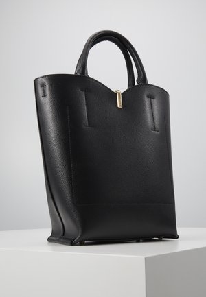 Czarna torebka z fakturowanej skóry z zaokrąglonymi uchwytami i małym złotym suwakiem, umieszczona na białym postumencie na neutralnym tle.