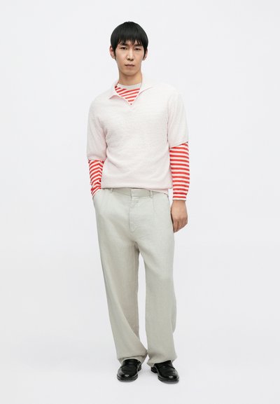 Φούξια ροζ πλεκτό κοντομάνικο πουλόβερ πάνω από κόκκινη και λευκή ριγέ μακρυμάνικη μπλούζα, συνδυασμένο με ανοιχτό μπεζ παντελόνι και μαύρα παπούτσια.