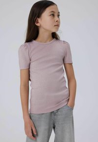 Lyserød, ribbet striktrøje med korte puffærmer og rund hals. Båret med grå, løst siddende jeans, hænderne i lommerne, neutral baggrund.