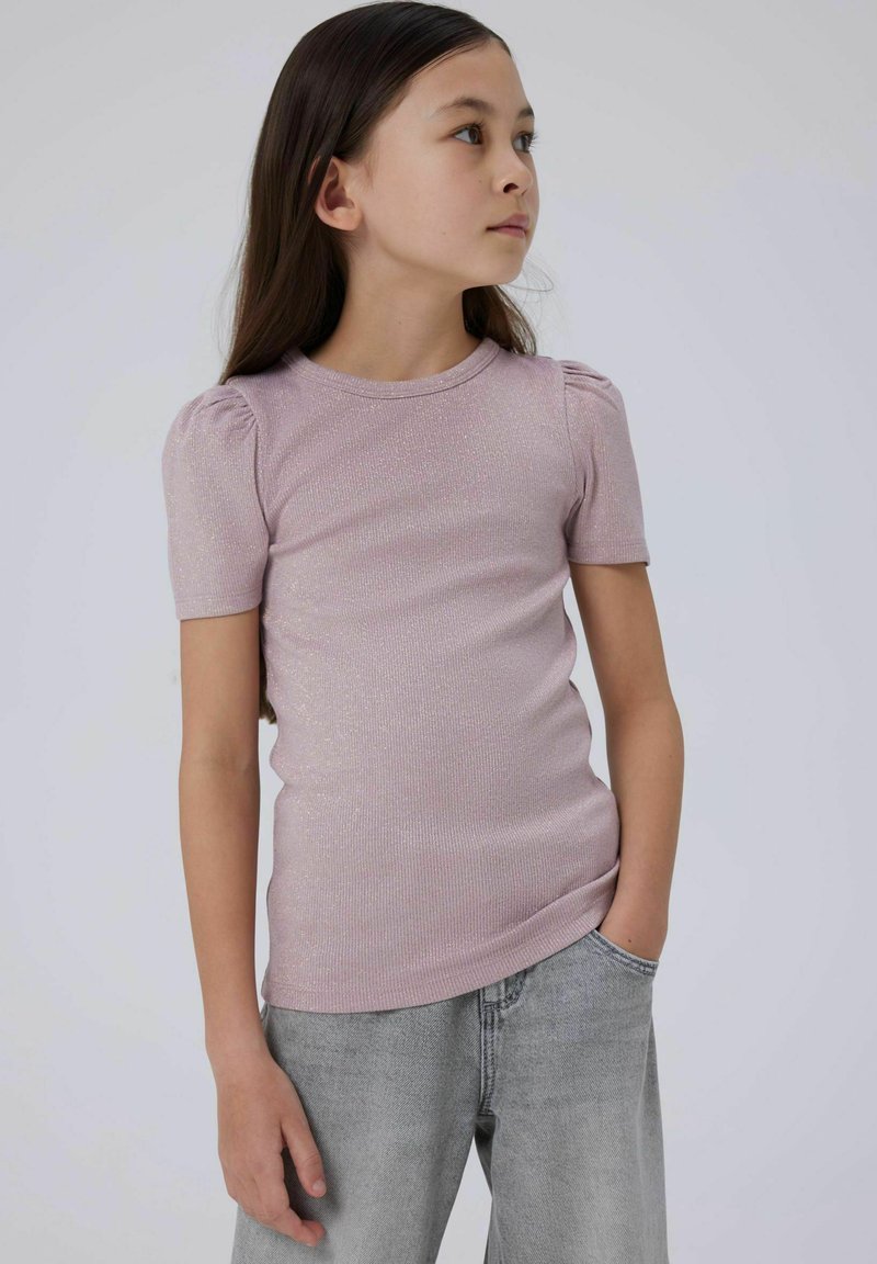 Lyserød, ribbet striktrøje med korte puffærmer og rund hals. Båret med grå, løst siddende jeans, hænderne i lommerne, neutral baggrund.