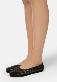 Ballerines en mesh noir avec un bout rond et un design ouvert, présentant une surface texturée et une semelle flexible. Convient à une utilisation décontractée.