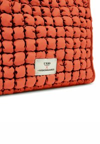 Borsa rettangolare in tessuto rosso testurizzato e imbottito. Presenta una placca con logo in argento nella parte inferiore che recita "UNIO HAMBURG X LES VISIONNAIRES."