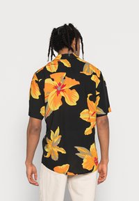 Korte mouwen shirt gemaakt van lichtgewicht stof, met een zwarte achtergrond en grote gele en oranje bloemenpatronen. Ontspannen pasvorm.