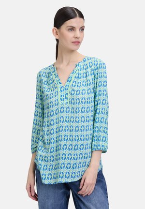 Una blusa leggera in blu e verde con un motivo geometrico, scollatura a V e maniche a tre quarti. Tessuto liscio con una leggera lucentezza.
