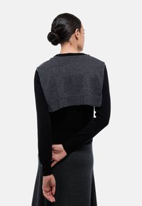 Haut noir à manches longues avec un pull court gris par-dessus, offrant une texture lisse et une coupe ajustée. Porté avec une jupe grise.