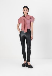 Black, fitted faux leather leggings paired with a light pink fitted top and a red gingham checked scarf tied around the shoulders. Chunky black shoes.