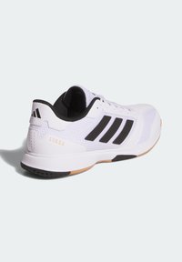 Baskets blanches avec accents noirs, tige en mesh et semelle en caoutchouc. Présente des rayures Adidas et le texte "LIGRA" sur le talon.