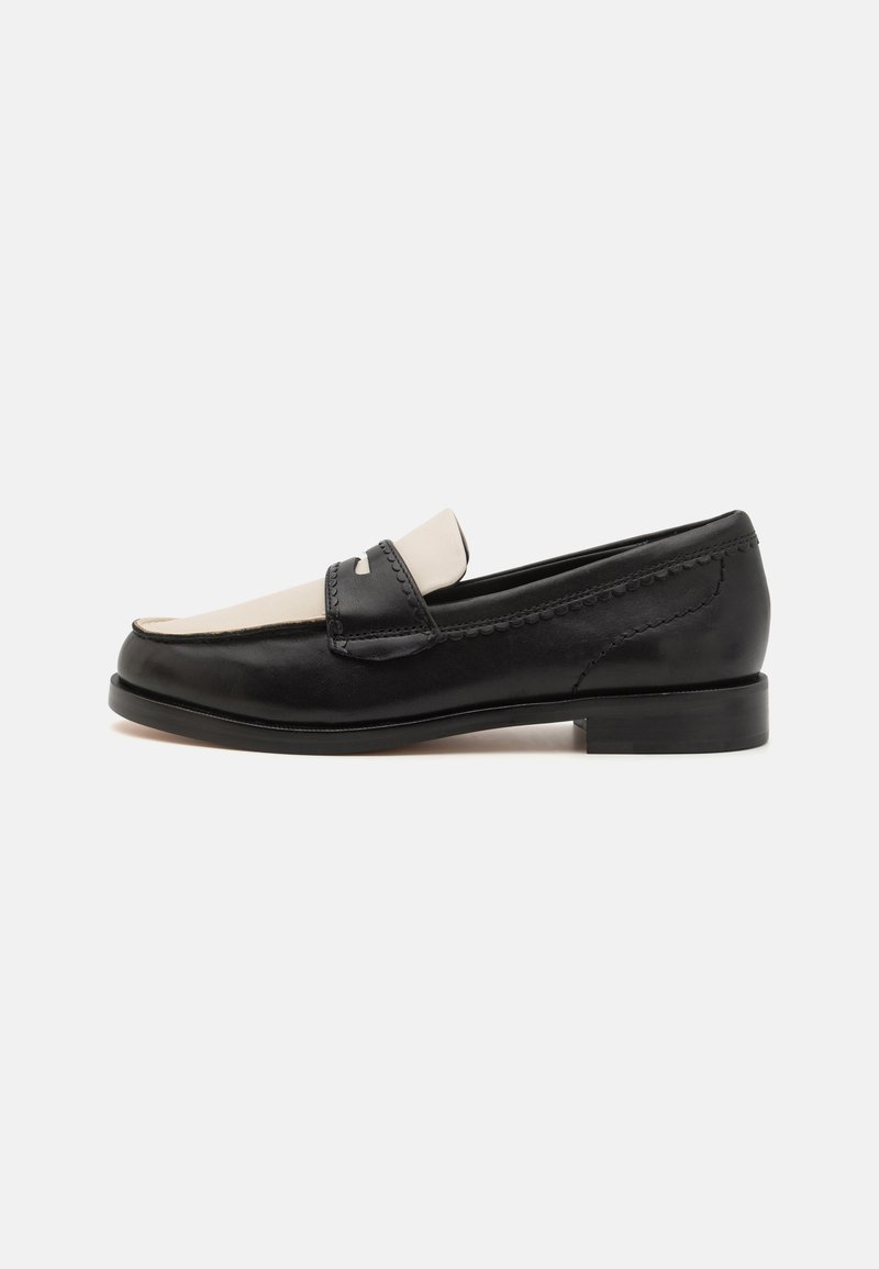 Mocassin en cuir noir avec un design de selle beige contrastant, présentant un bout rond et un petit talon, des coutures détaillées et un profil élégant.