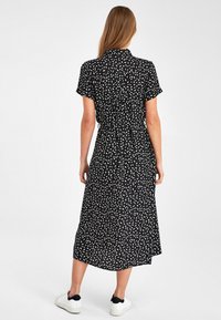 Czarna sukienka midi z krótkimi rękawami, białym abstrakcyjnym wzorem, kołnierzykiem, taliowanym krojem i delikatnymi zakładkami, zestawiona z białymi trampkami.