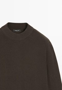 Maglione marrone a coste con scollo alto e arrotondato. Presenta una texture liscia e un'etichetta sul collo con il nome del marchio.