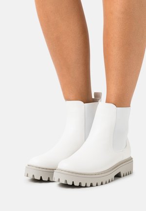 White ankle boots made of smooth leather, featuring a thick gray rubber sole with a serrated edge and elastic side panels for ease of wear.