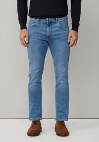 Jeans de denim azul claro con un corte recto, diseño de cinco bolsillos y cierre de botón de metal, combinados con zapatos de ante marrón.