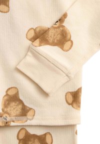 Beige pyjamas stof med et gentaget mønster af bamser i nuancer af brun. Blød tekstur med ribbede manchetter og ren syning.