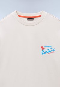 Beige genser med ribbestrikket rund hals, med en blå og rød logo som står "Cortina DOLOMITI." Myk bomullstekstur.