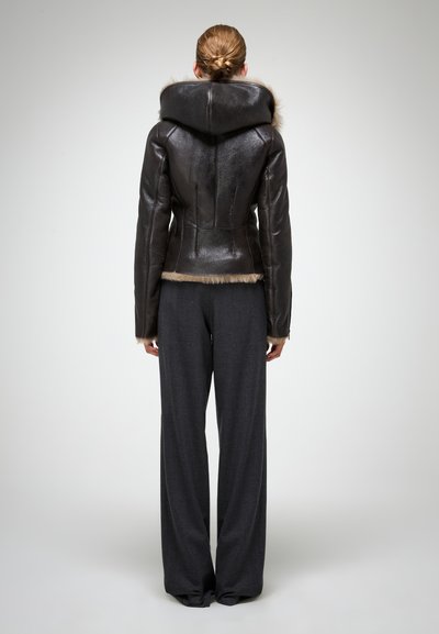 Braune Lederjacke mit einer großen, mit Fell gefütterten Kapuze, schlanker Passform und kontrastierendem Fellbesatz am Saum. Kombiniert mit weit geschnittenen grauen Hosen.