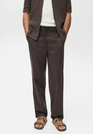 Pantaloni larghi di colore marrone scuro, leggeri, con cintura elastica e cordoncino, abbinati a una maglietta neutra e sandali marroni.