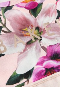 Tkanina s cvjetnim uzorkom koja prikazuje velike ružičaste i ljubičaste cvjetove na svijetloružičastoj pozadini s zlatnim natpisom "BAKER by Ted Baker." Glatka tekstura.