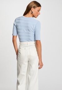 Haut en tricot côtelé bleu clair à rayures horizontales et à manches courtes. Associé à un pantalon blanc taille haute avec des poches arrière.