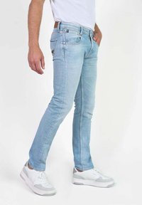 Jeans skinny de denim azul claro con un diseño de cinco bolsillos, ligeras desgastados y una cintura de altura media, combinados con zapatillas blancas.
