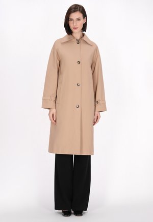 Beige trenchcoat met een kraag, knopen aan de voorkant en lange mouwen. Beschikt over zijzakken en is gecombineerd met zwarte wijde broekspijpen.