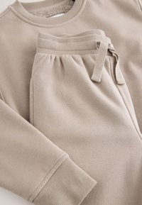 Sweatshirt and sweatpants set in light beige. Soft cotton material, ribbed cuffs and waistband, adjustable drawstring on pants, casual design.