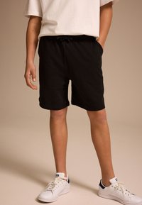 Black shorts with an elastic waistband and drawstring, made from soft material. Paired with white sneakers featuring navy accents.