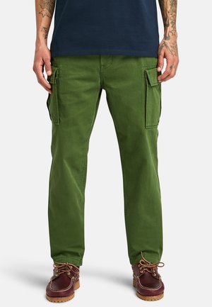 Green cargo pants made of cotton with side pockets, straight-leg design, and a soft texture, paired with brown shoes featuring laces.