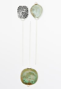 Trois épingles décoratives avec des tiges en métal. La partie supérieure a un carré à motifs noir et blanc, celle du milieu a une forme arrondie de couleur vert clair, et la partie inférieure est une plus grande pièce arrondie de couleur vert terre avec un accent en perle.