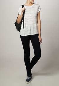 Bílý krátký rukáv top s texturovaným, pruhovaným vzorem; spárovaný s černými skinny džínami a tmavě modrými teniskami. Černý batoh na rameni.