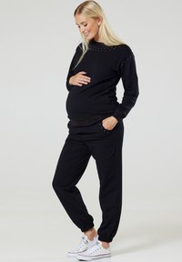 Crni set majice za trudnoću i jogger hlača s ukrasnim čavlima, elastičnim manžetama i bočnim džepovima, izrađen od mekanog materijala za udobnost.