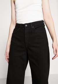 Schwarze Jeans aus Denim mit hoher Taille und geradem Bein, ausgestattet mit Vordertaschen, einem Knopfverschluss und kontrastierenden Nähten.