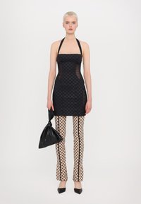 Rochie halter neagră cu părți transparente, asortată cu pantaloni crem cu model alb și negru. Modelul ține o poșetă neagră, legată. Pantofi negri lucioși.